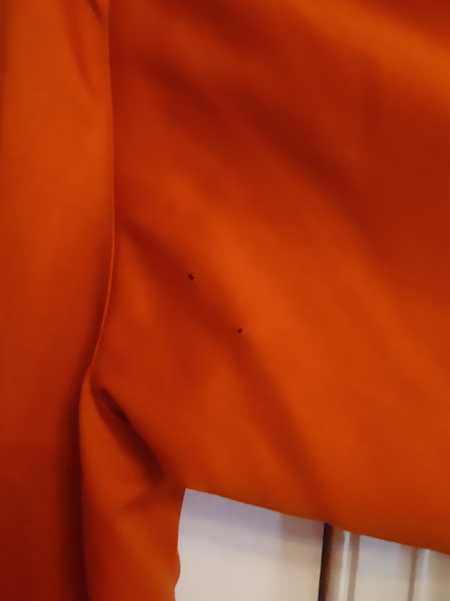 Close-up of back of the orange coat’s sleeve with two small pinholes visible. 